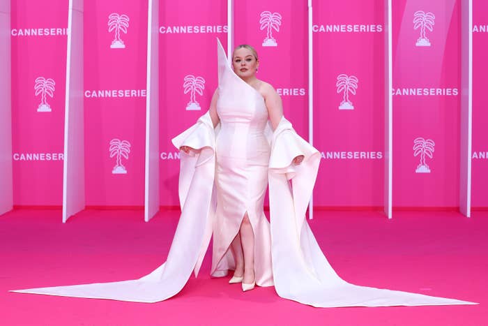 Person in an elegant, dramatic gown with long, flowing sleeves on a red carpet at a Cannes event, posing for photos