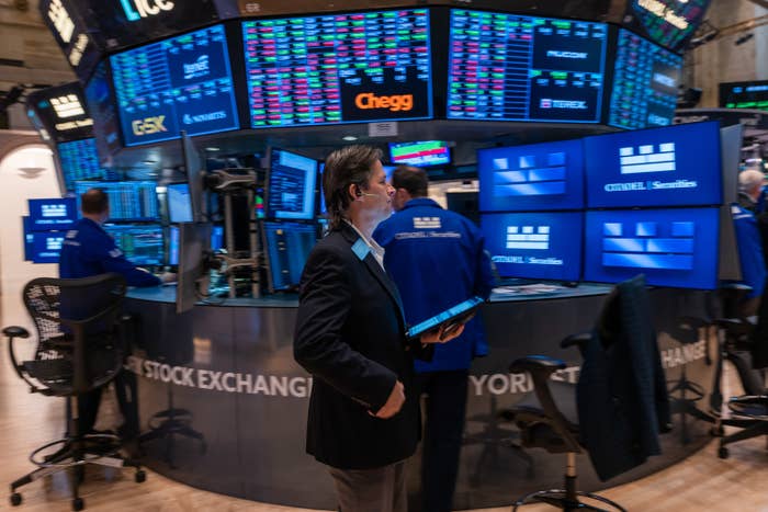 Stock exchange traders work at desks full of monitors displaying market data