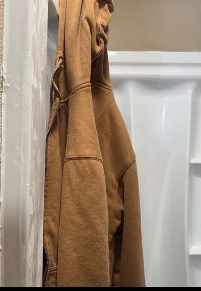 A brown hoodie is hanging on a shower wall, with a white shower background