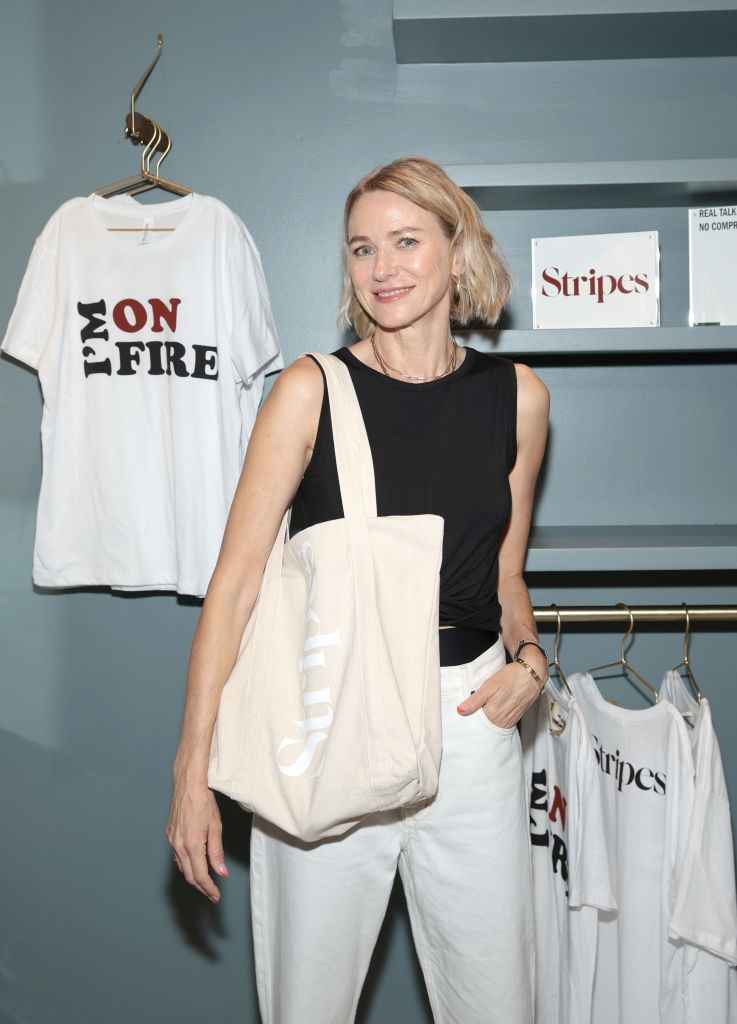 Person in casual outfit with a tote bag, standing beside graphic T-shirts on display