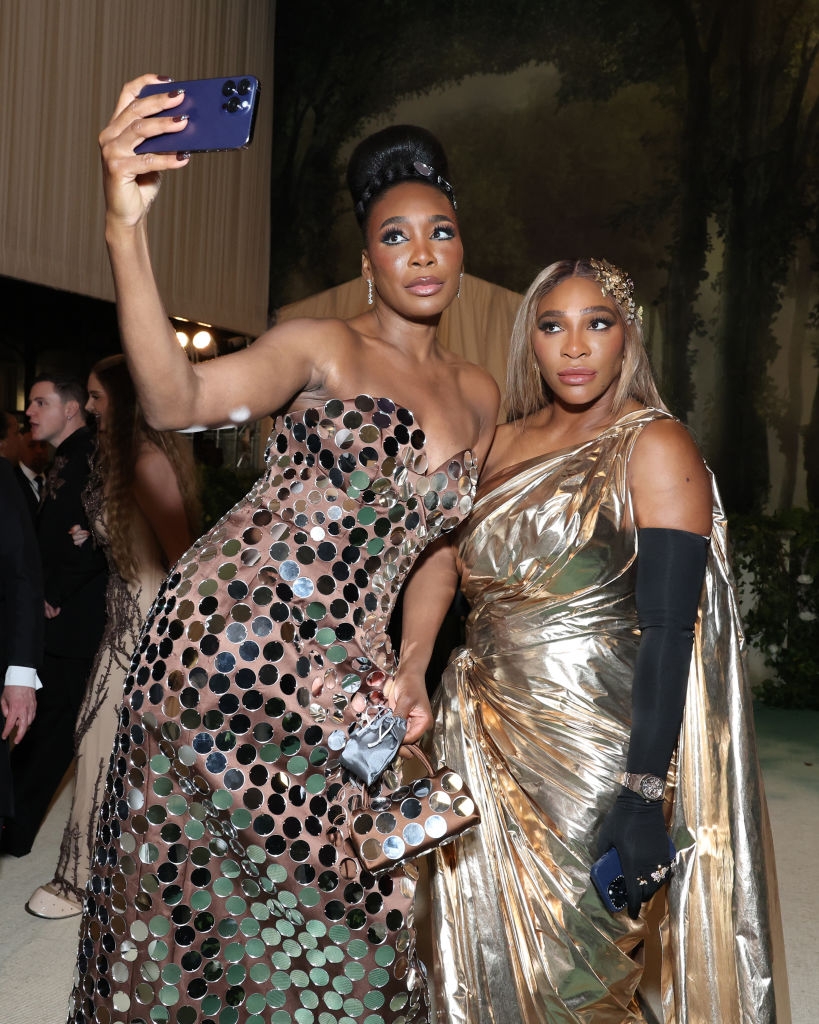 Venus and Serena posing for a selfie in elaborate gowns