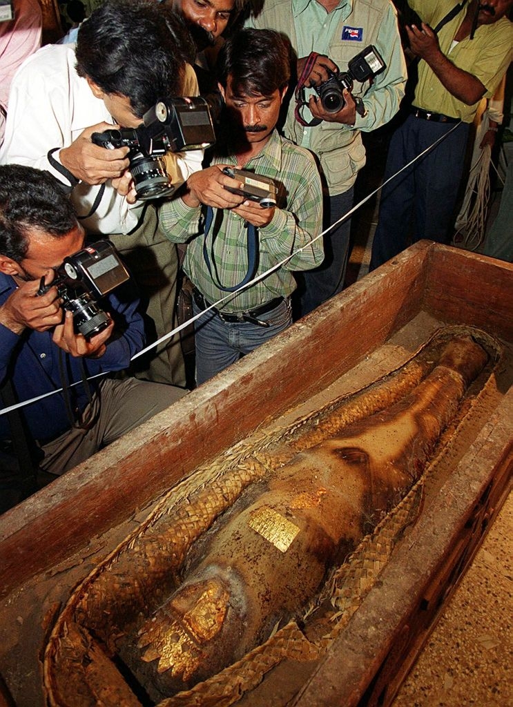 Photographers take close-up shots of an ancient mummy inside an open sarcophagus on display