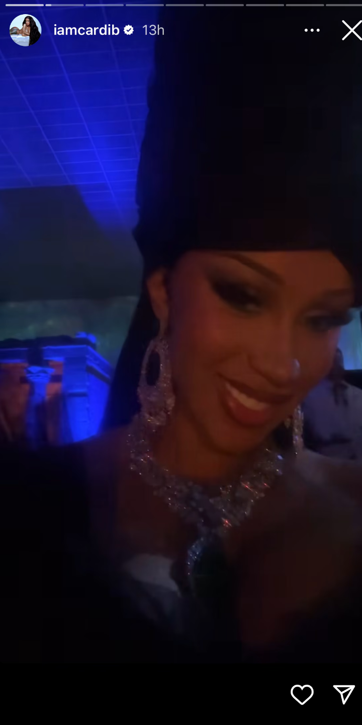 Cardi wearing a head wrap and elegant jewelry, smiling in a dimly lit setting