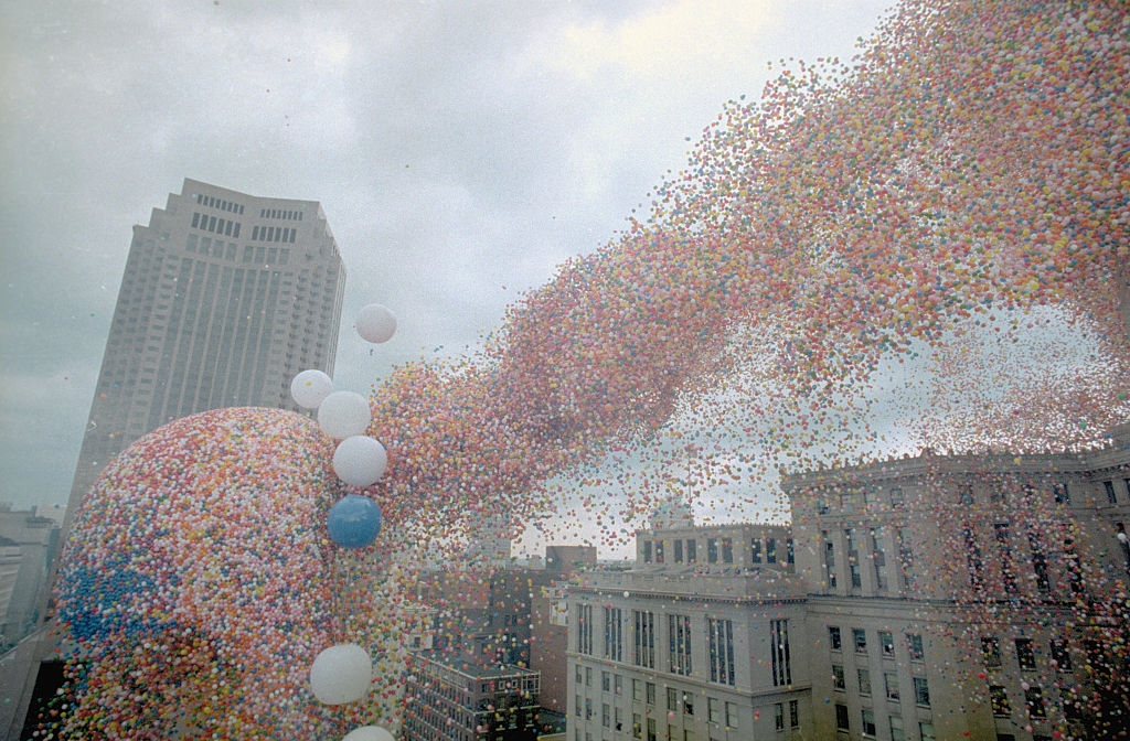 Massive balloon release over a cityscape with tall buildings in the background, creating a colorful airborne spectacle