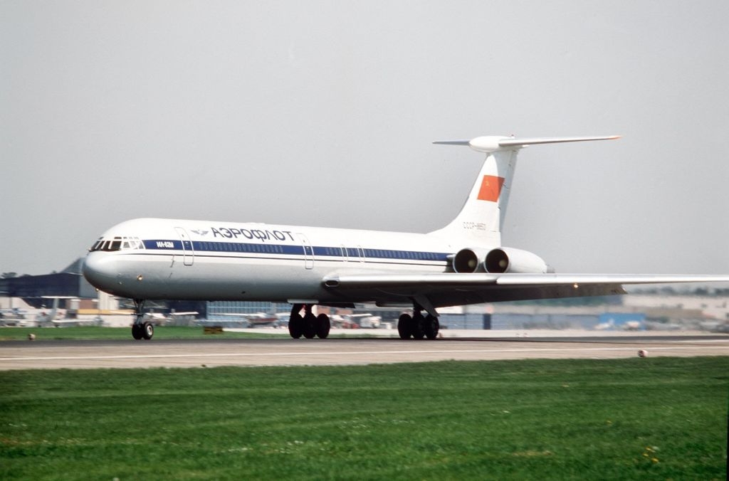 Commercial airplane taxiing on a runway at an airport, with airport buildings visible in the background