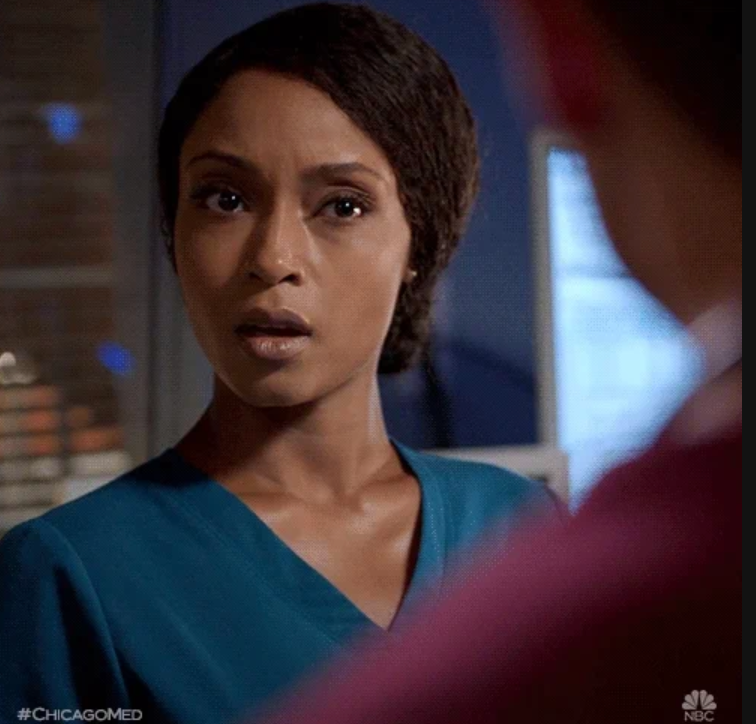 Person in a medical setting looks surprised, wearing a teal scrub top. Interacting with another person off camera
