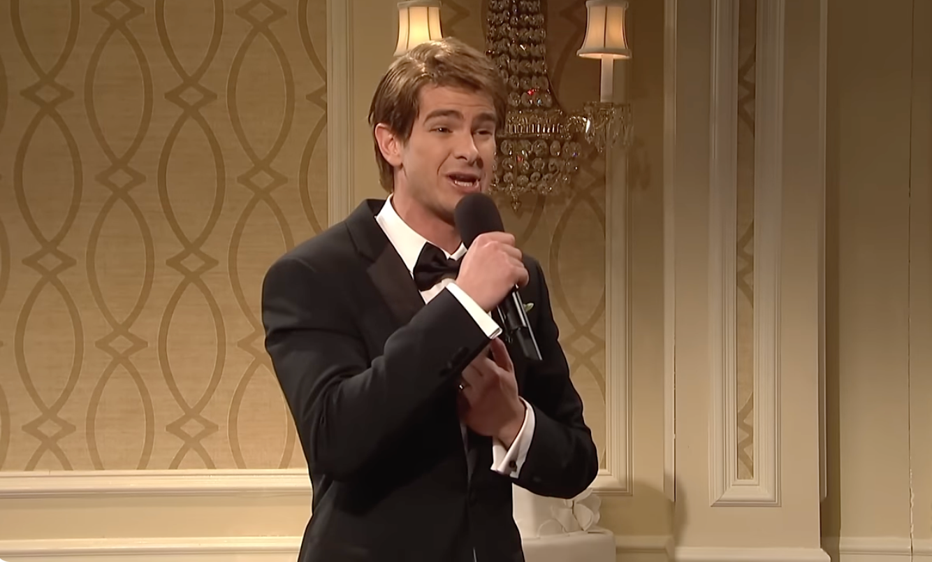 Person in a tuxedo holding a microphone sings indoors at a formal event, possibly a wedding setting