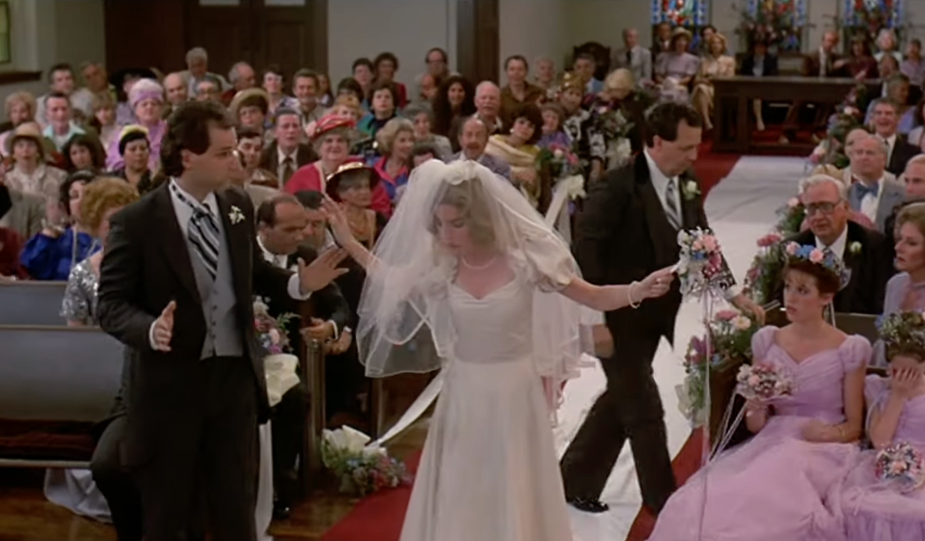 Bride in a classic gown walks down the aisle with surprised guests and ushers at a wedding ceremony, capturing a moment of commotion and curiosity