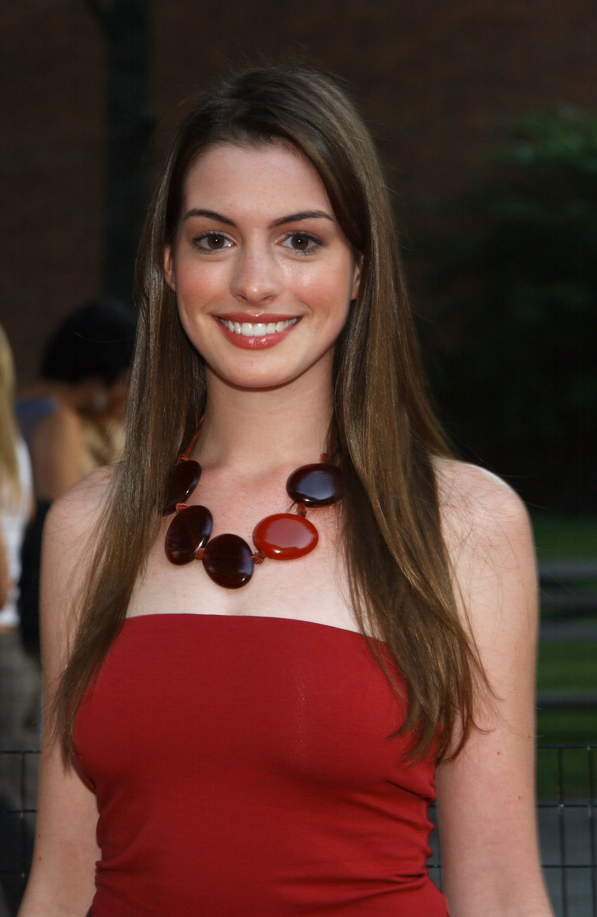 A woman in a strapless dress with a chunky statement necklace smiles at an outdoor event