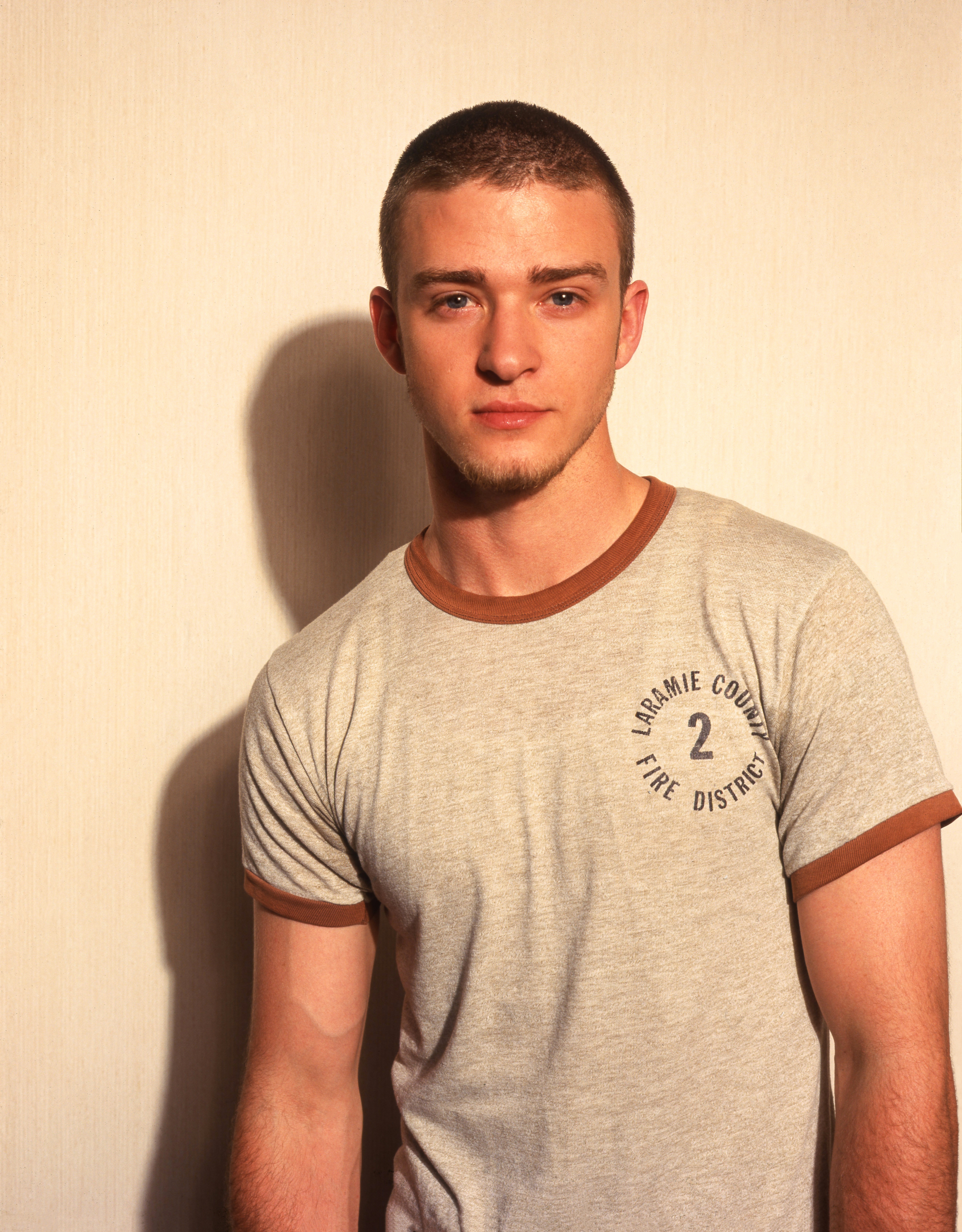 Person in a casual T-shirt with short hair poses in front of a plain backdrop