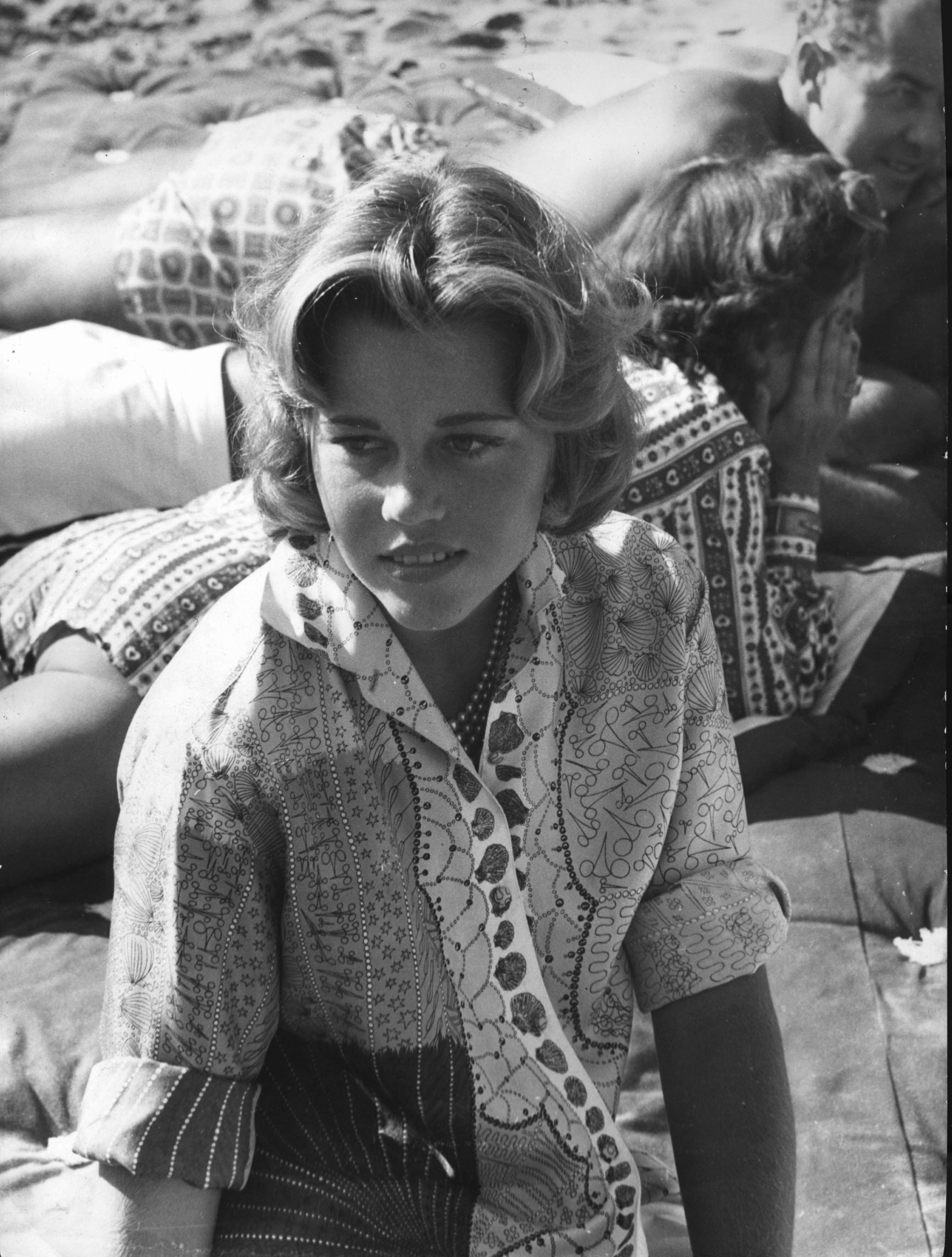 Person lounging on a beach, wearing a patterned shirt. Others are relaxing in the background