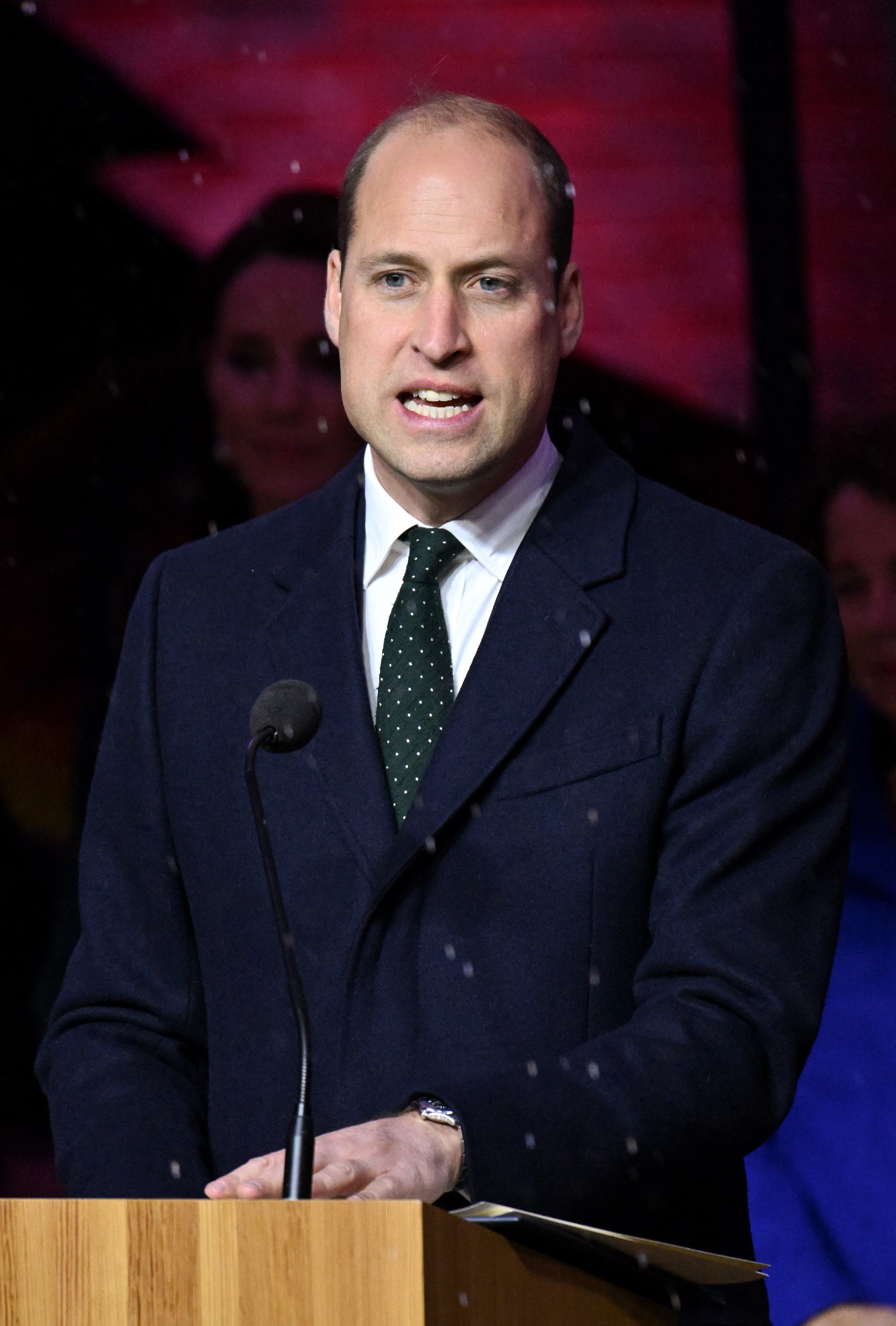 A person in a formal suit speaks at a podium during an event