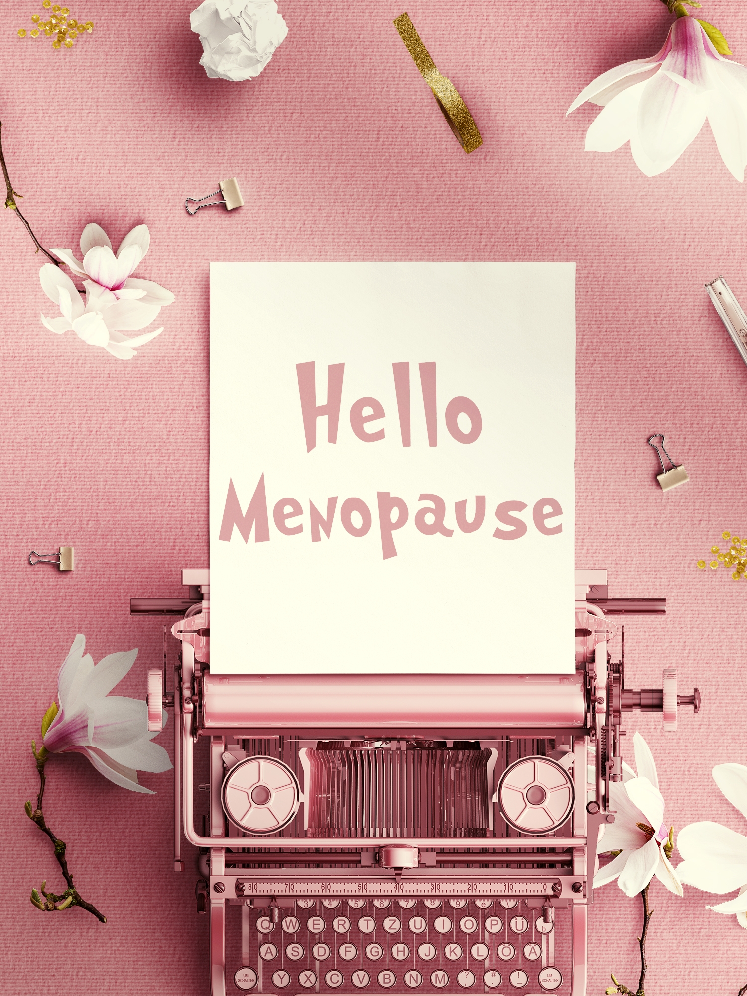 Typewriter with a paper reading "Hello Menopause," surrounded by flowers and stationery items on a flat surface