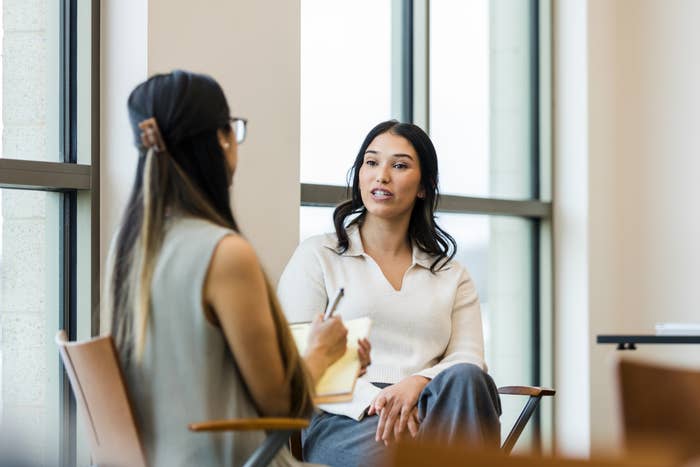 Two people having a serious conversation in an office setting. One is taking notes on a notepad while listening intently