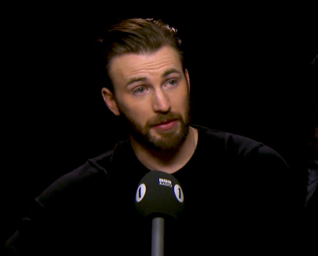 A man speaking into a microphone during an interview, wearing a casual dark top