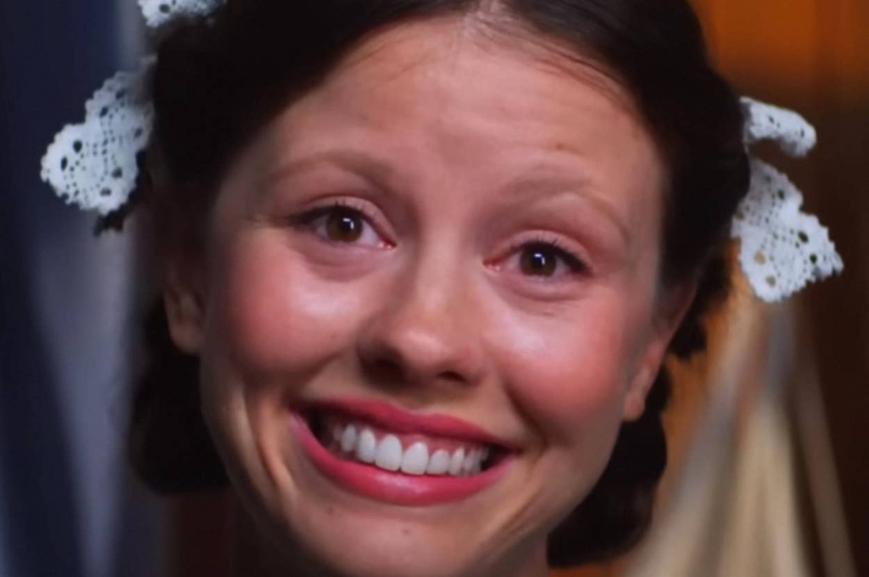 Person with a wide smile and lace hair accessories, likely in a vintage movie or show setting