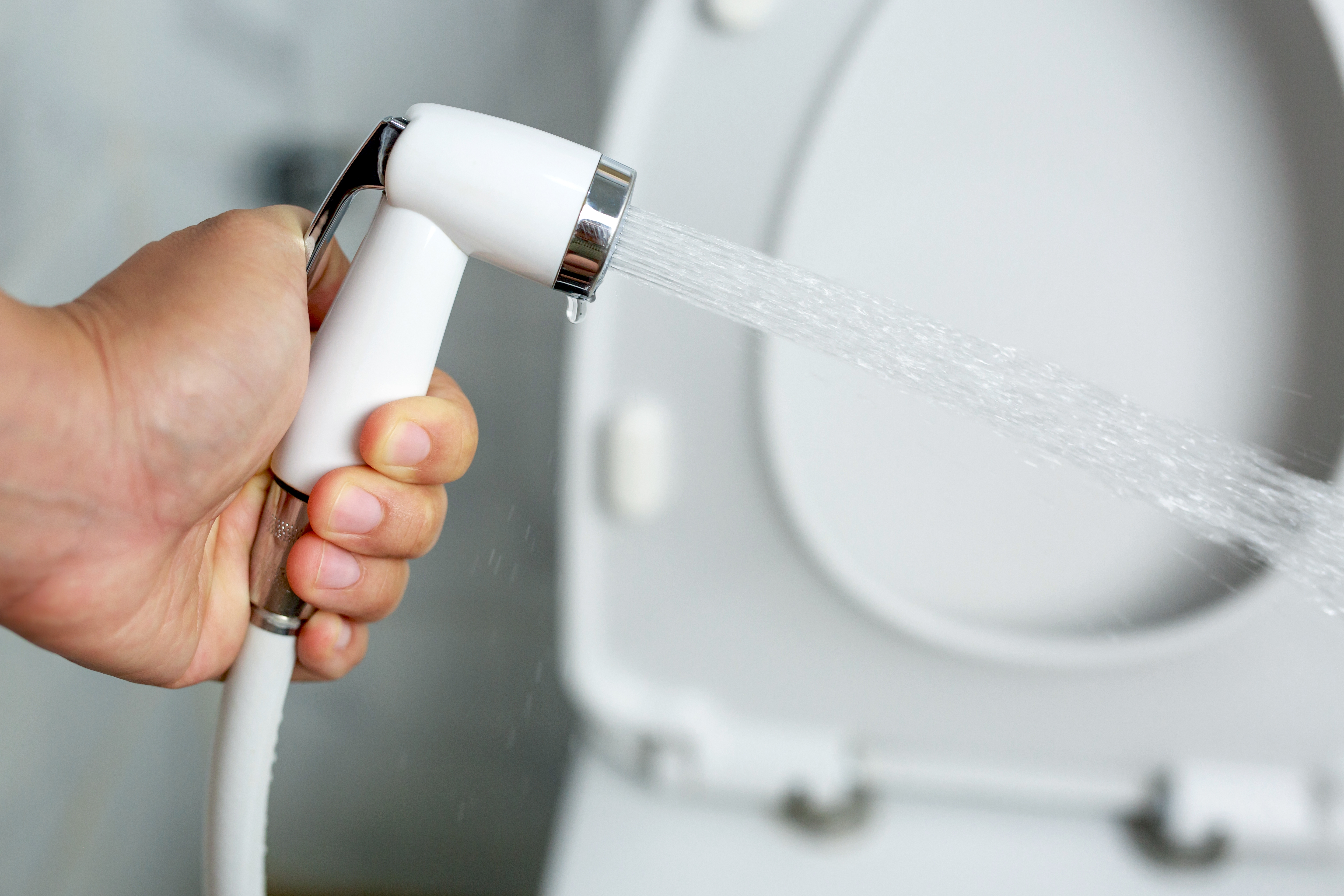 En hånd som holder en bidet -sprøyting, vann som strømmer mot et åpent toalettsete