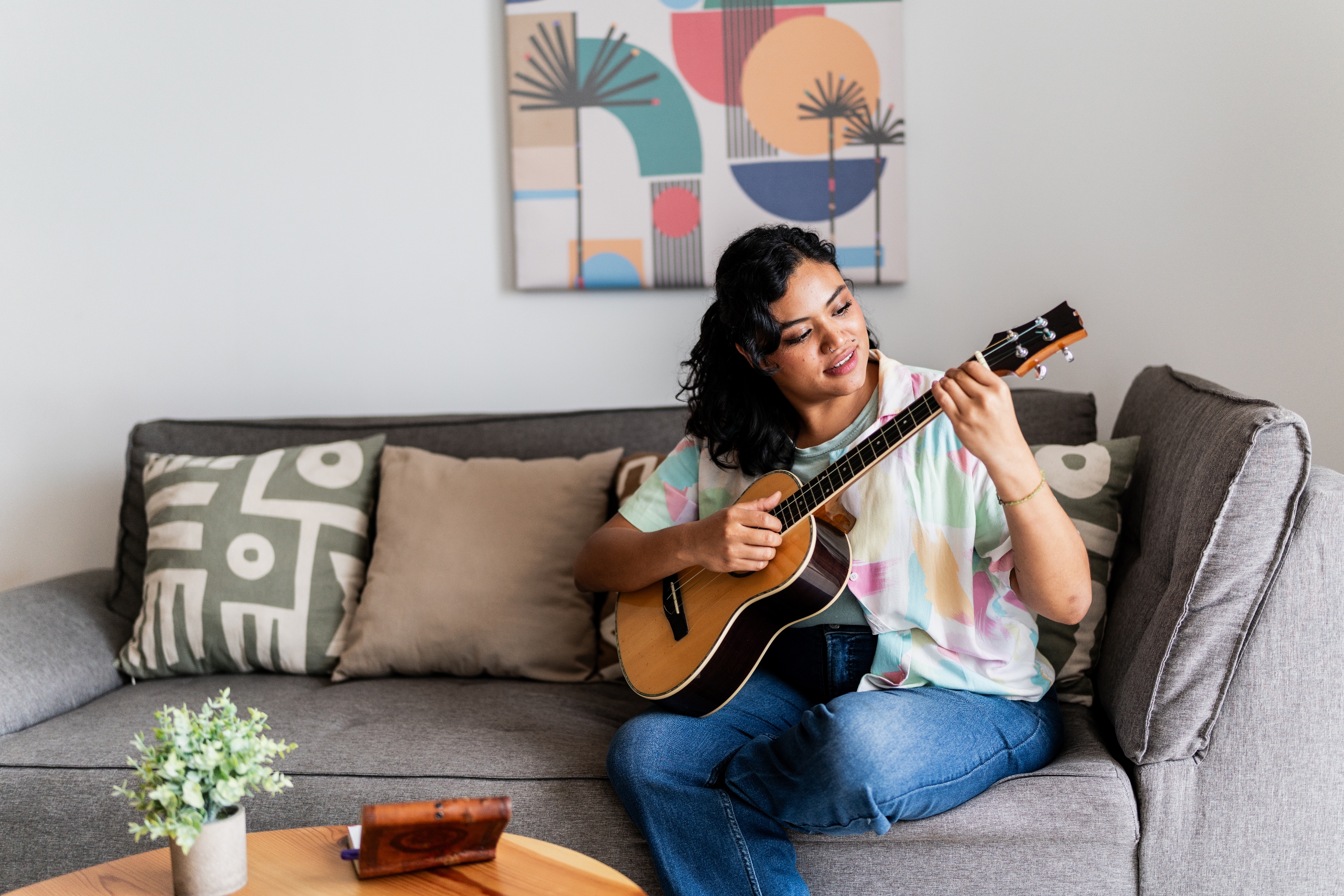Person som sitter på en sofa, spiller en gitar, med abstrakt kunstverk på veggen