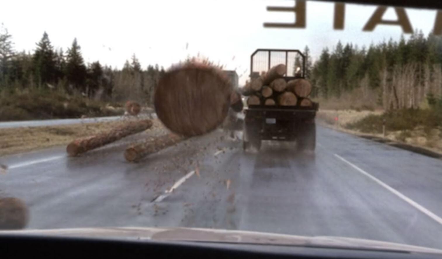 Scene from a movie or TV show with logs falling off a truck on a forested highway, creating a sense of danger