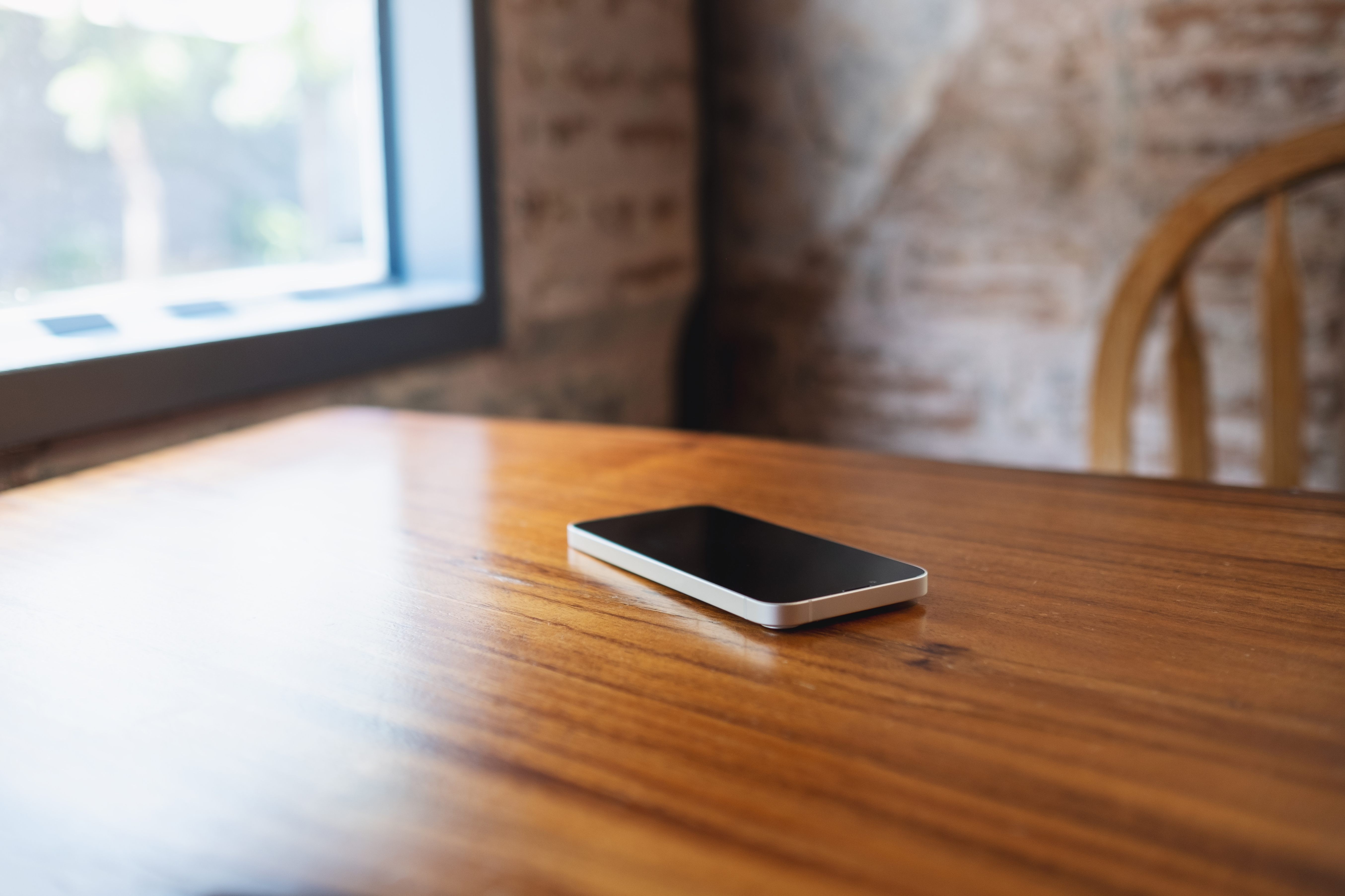 Smarttelefon på et trebord i nærheten av et vindu, i et rom med en murvegg og en trestol
