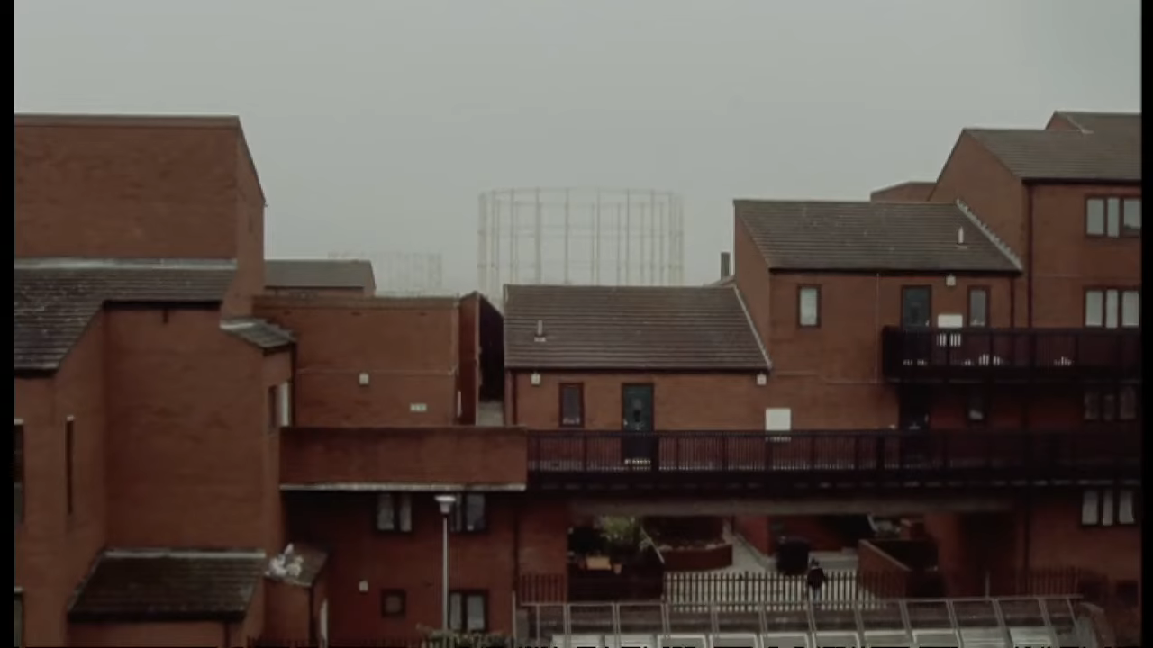 A view of several brown brick buildings with modern architectural design and visible stairways, set against a cloudy sky