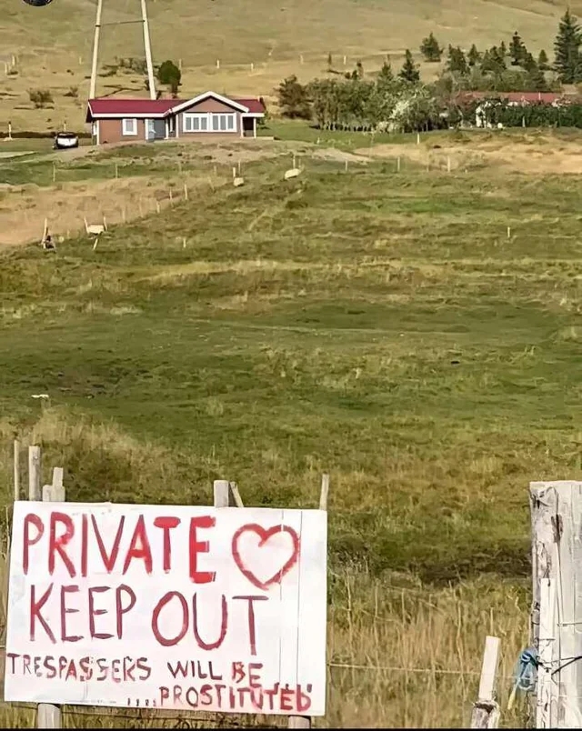 Sign on a rural property reads: "Private Keep Out. Trespassers Will Be… Prostituted," against a backdrop of fields and a house