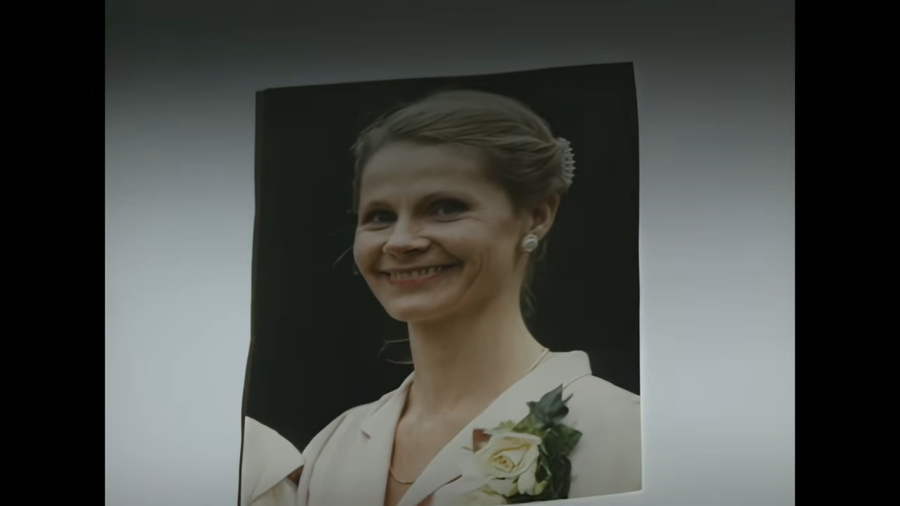 Smiling woman in a dress shirt with floral detail looks at the camera against a plain background