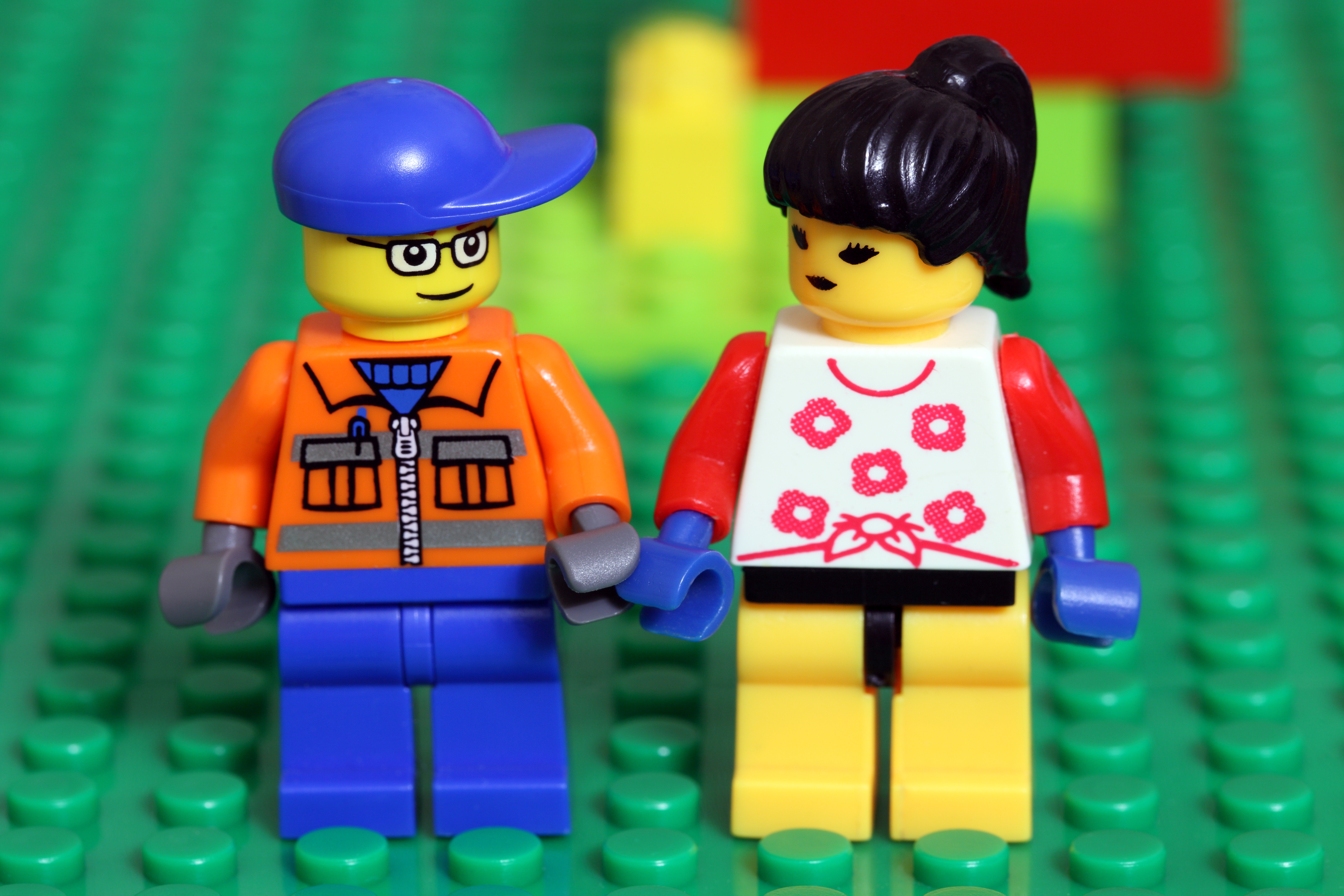 Two LEGO figures on a green baseplate: one in a cap and jacket, the other in a floral top with a ponytail