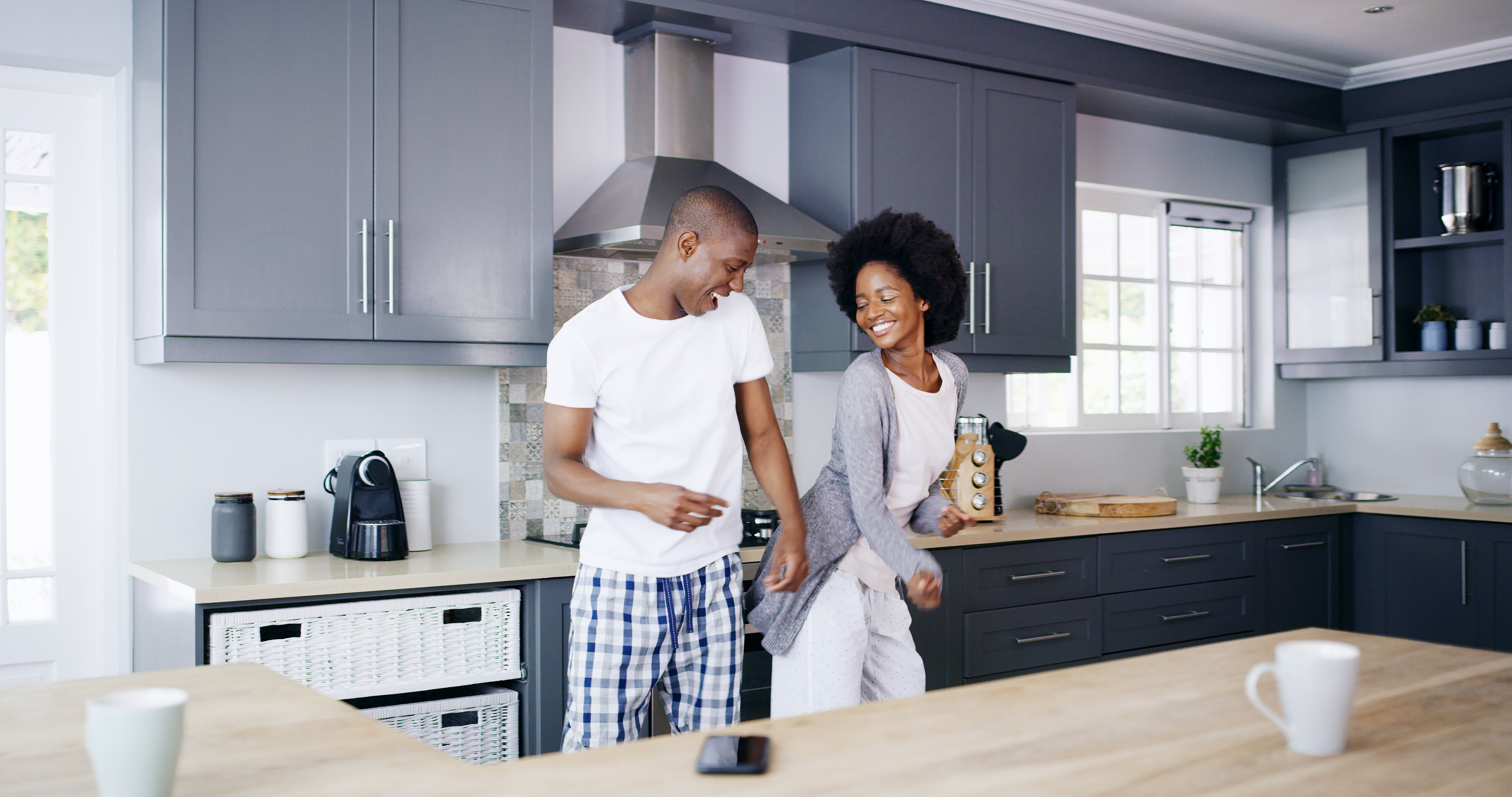 A smiling couple dances playfully in a modern kitchen, surrounded by sleek cabinets and appliances
