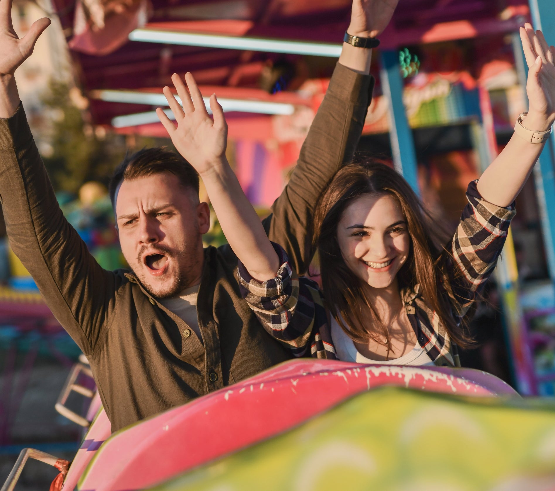 Two people on a carnival ride, excitedly raising their hands and smiling, enjoying a fun day out