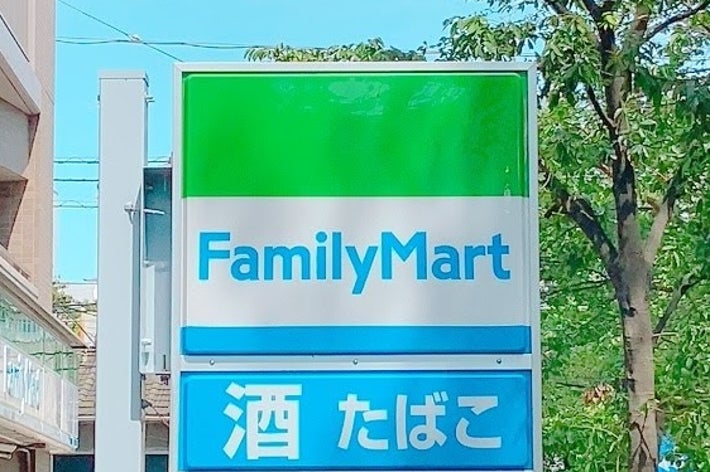 ファミリーマートの看板、酒とたばこの案内。周囲に建物と木々が見える。