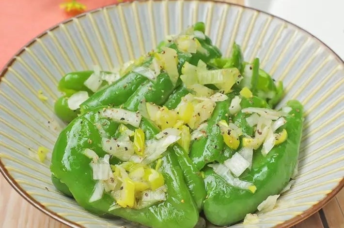 お皿に盛られた調理済みの緑のピーマンと刻んだ玉ねぎ、胡椒が振られ、美味しそうな料理が並ぶ。