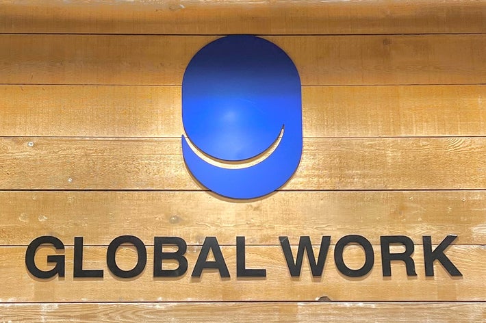 木製の壁に掲げられた「GLOBAL WORK」のロゴ。上部に青いシンボルがある。