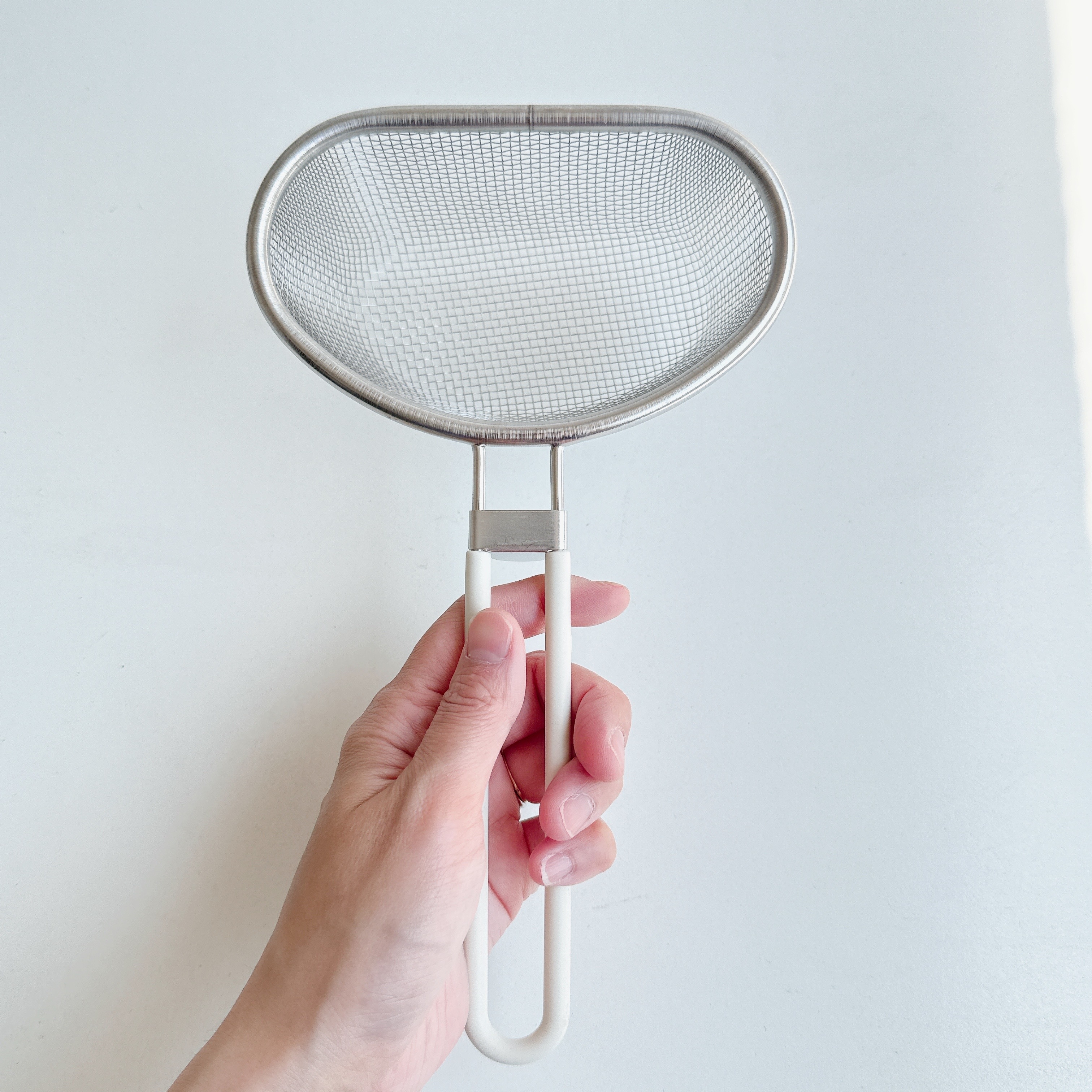 手に持たれた金属製のキッチン用ストレーナーの画像。