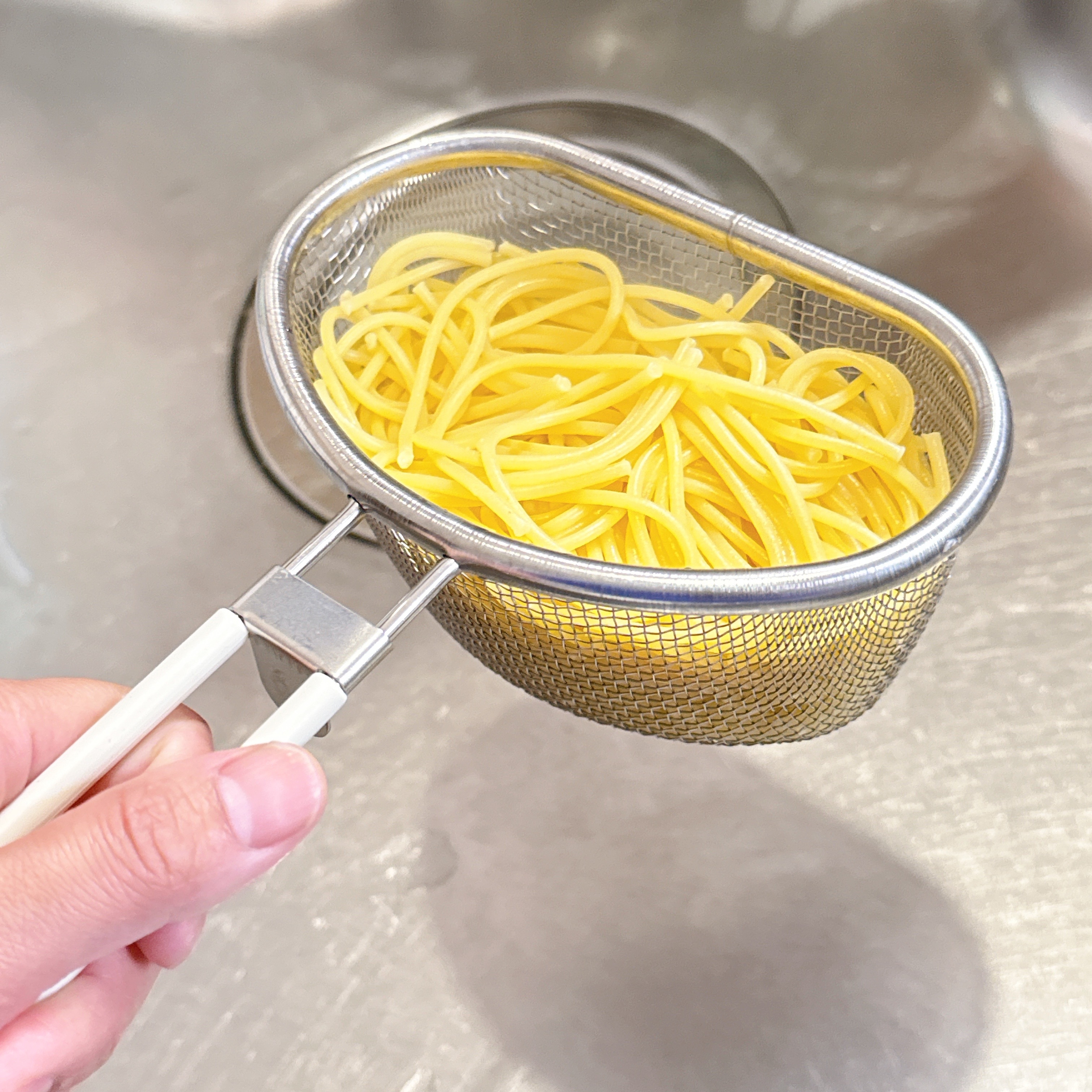 排水口で小さな金属製のザルに入っている茹でたスパゲッティ。