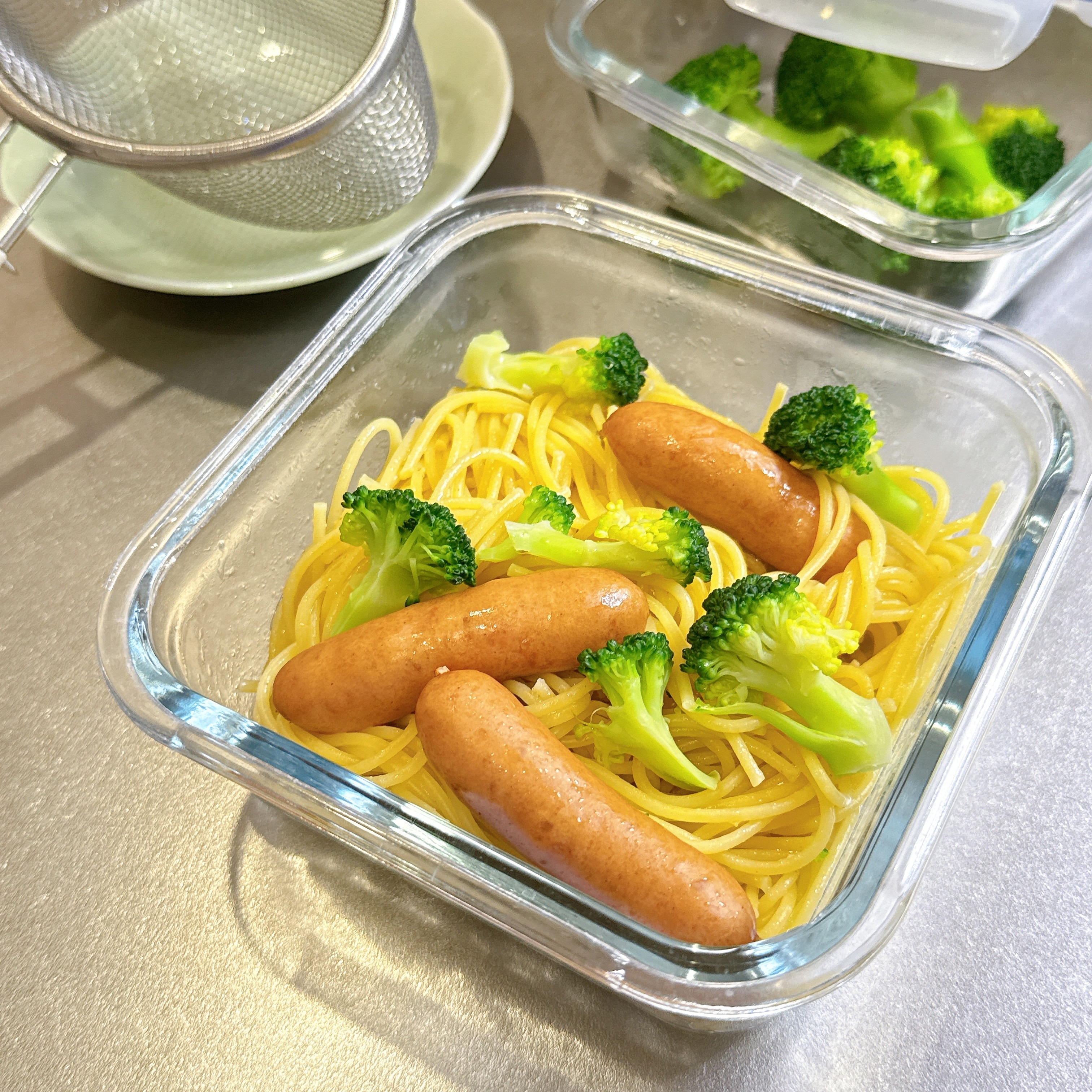 透明な容器にスパゲッティ、ソーセージ、ブロッコリーが入っている食事の準備。隣にブロッコリー入りの別の容器。