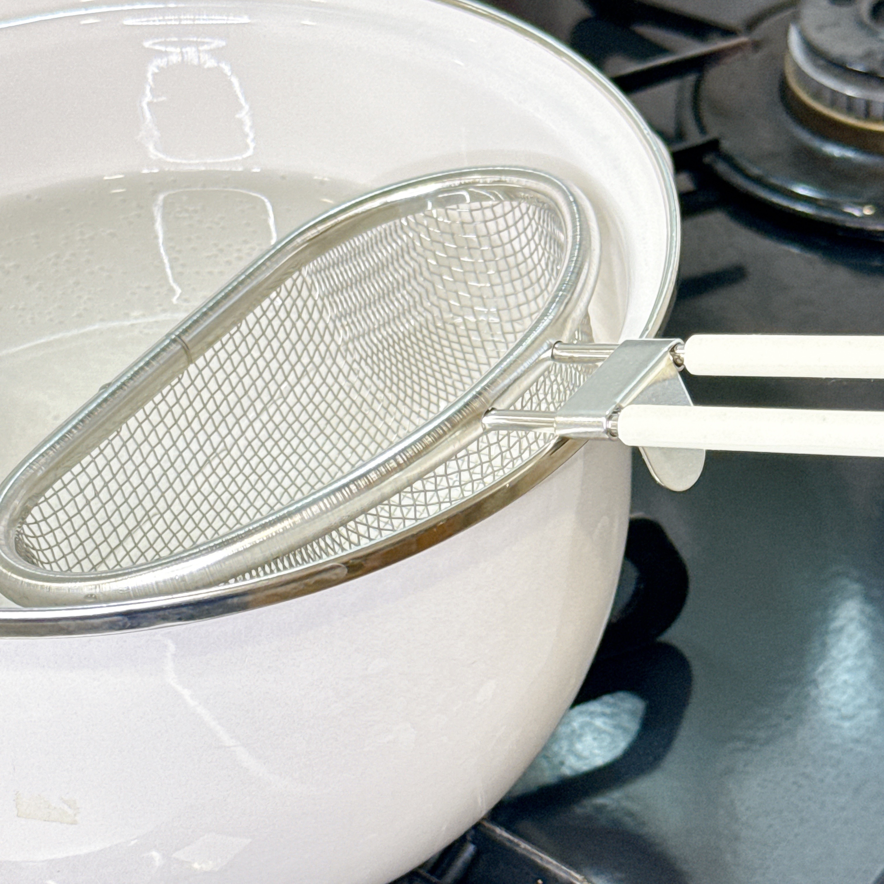 鍋で沸かしたお湯に金属製のザルが入っているキッチンシーン。