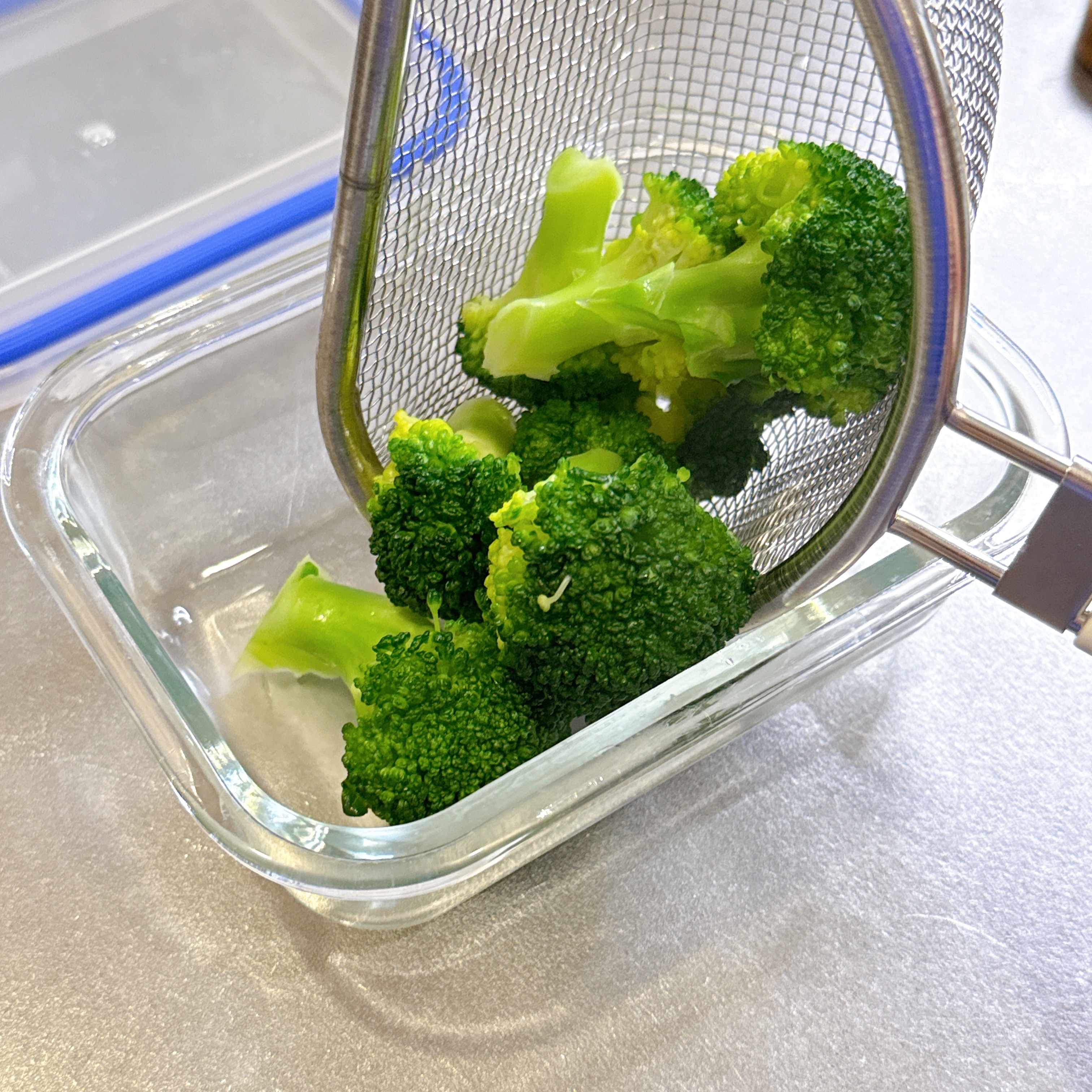 ザルを使ってブロッコリーをガラス容器に移しているところ。