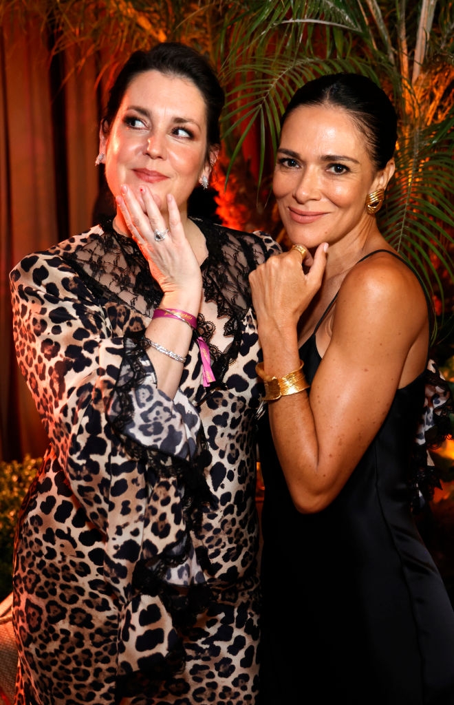 Two women posing at an event; one in a leopard print dress, the other in a sleek, sleeveless dress. Both have their hands near their faces, smiling