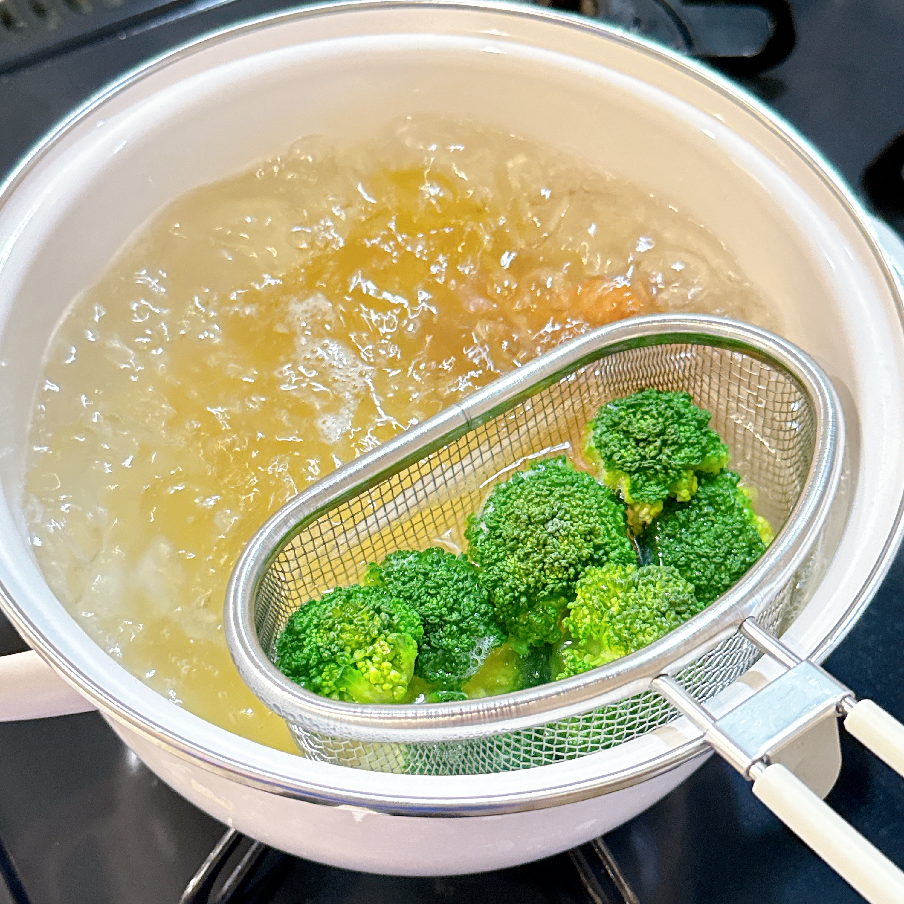 鍋でパスタを茹でながら別の器具でブロッコリーを茹でている。クッキングシーン。