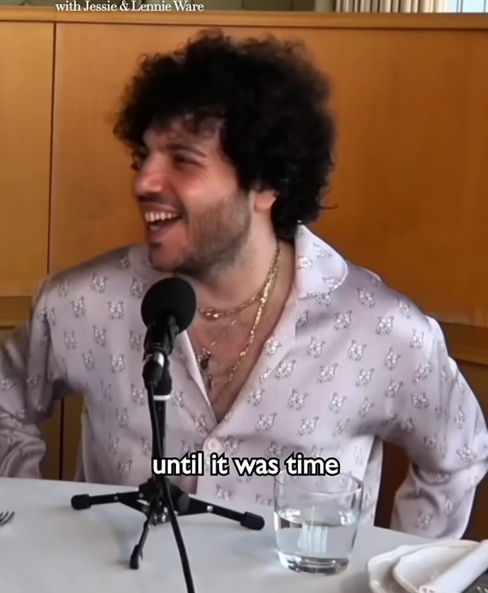 Person smiling while seated at a table, wearing a patterned shirt, with podcast microphones in front of them. Subtitles read: &quot;until it was time&quot;