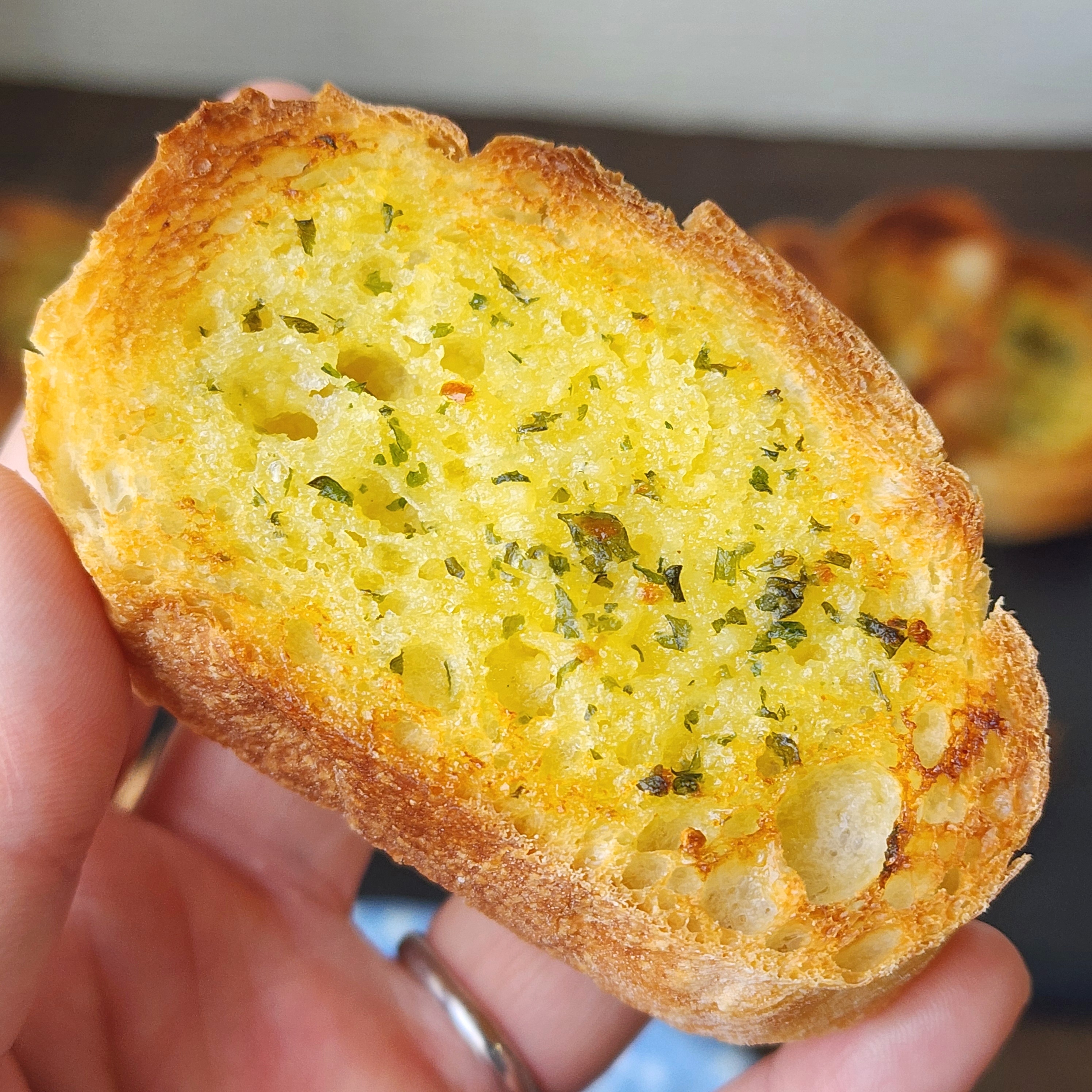 にんにくとハーブがのった焼きたてのガーリックトーストのクローズアップ。手で持たれている。