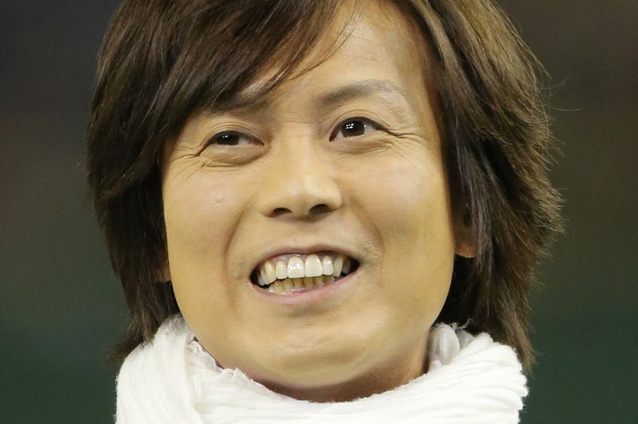 男性が白いスカーフを身に着けて笑顔を見せている。詳しい背景や状況は不明。