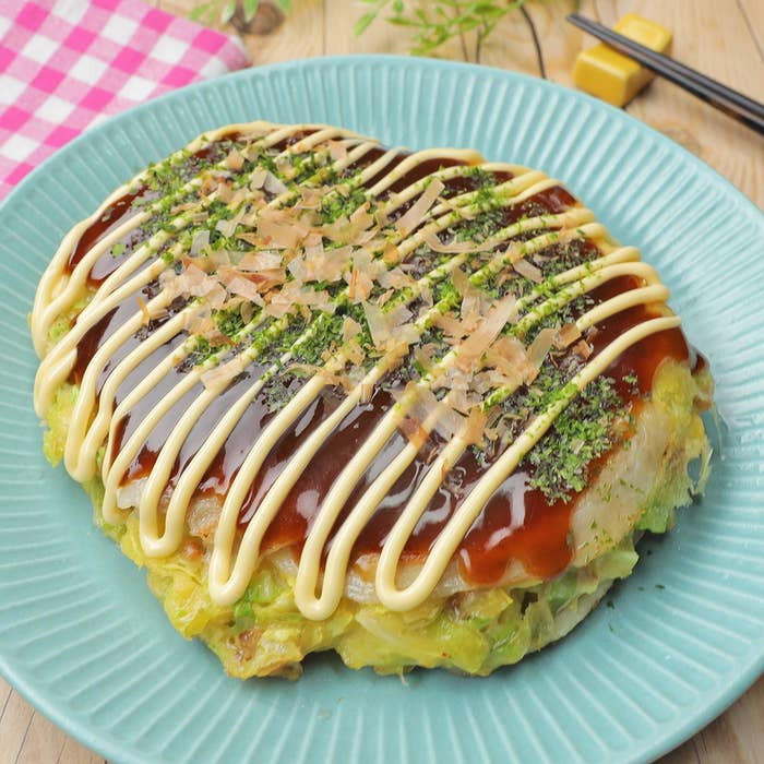 青い皿に盛られたお好み焼き、上にソース、マヨネーズ、鰹節が飾られている。