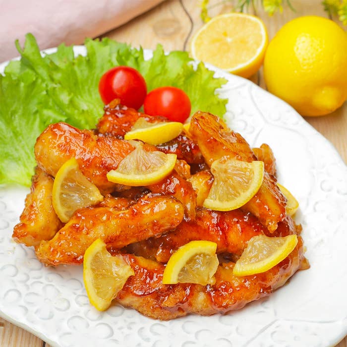 レモンの輪切りが乗った甘辛チキンウィングのプレート、緑の葉とミニトマト添え。美味しそうな料理のディスプレイ。