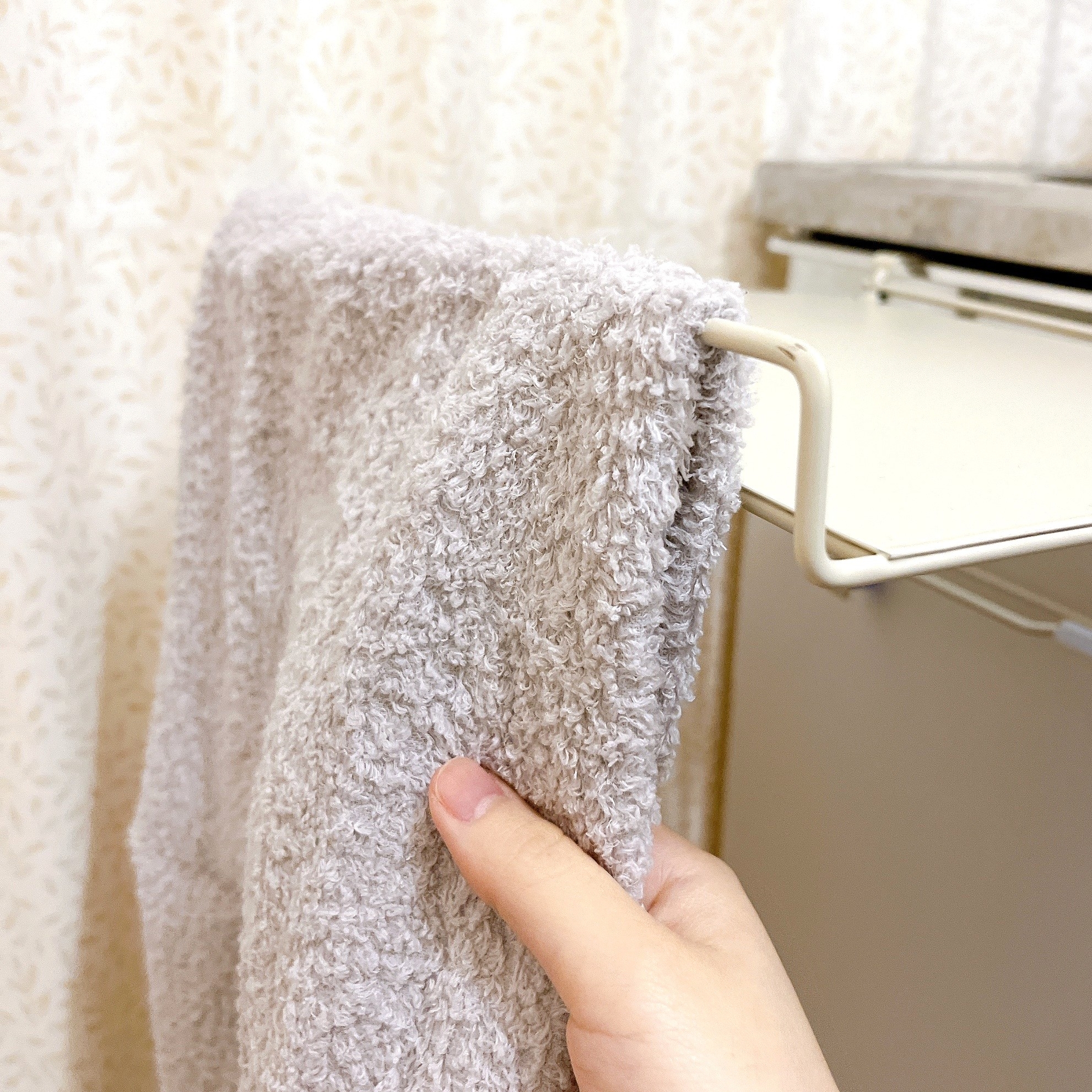 タオルをバーにかけている手。背景にカーテンが見える。