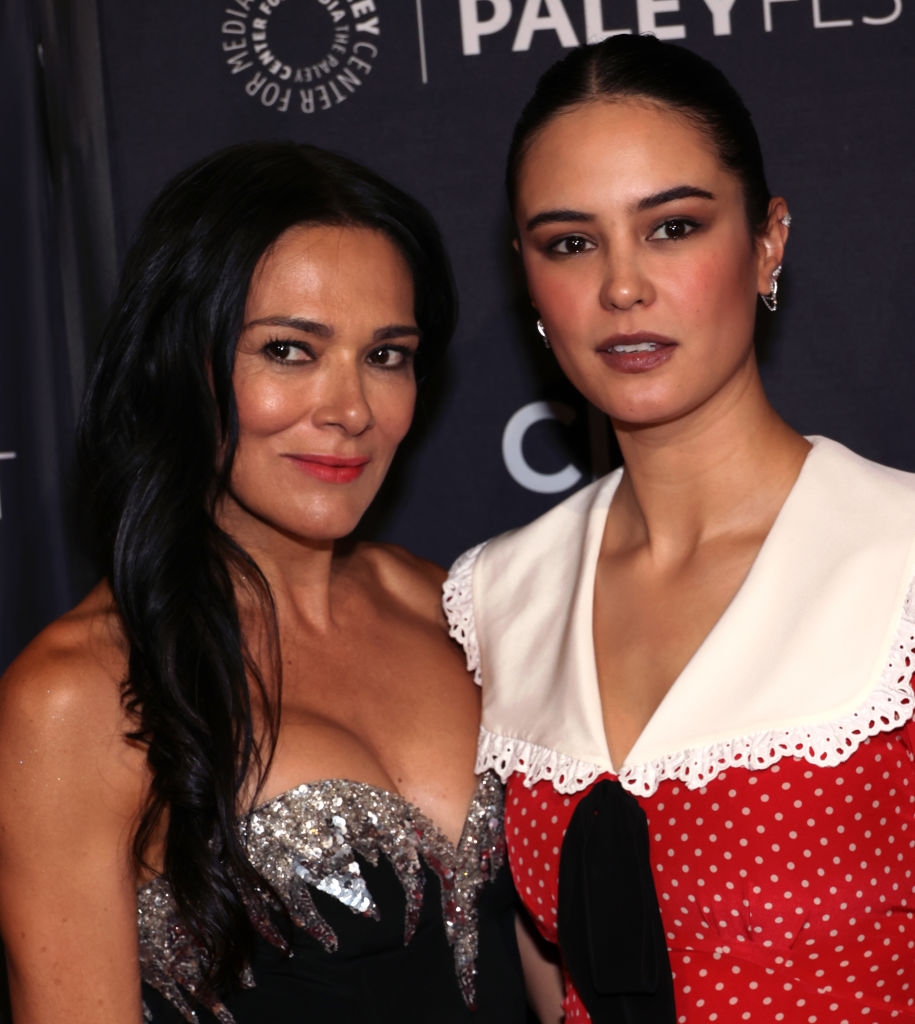 Two women at an event. One wears a glittering strapless dress; the other wears a dress with a white collar and polka dots