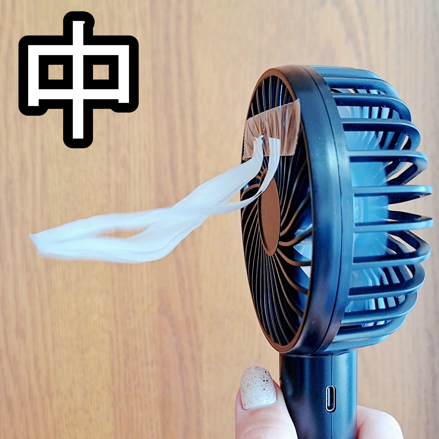 手に持たれた小型ファンをテープで固定した様子。