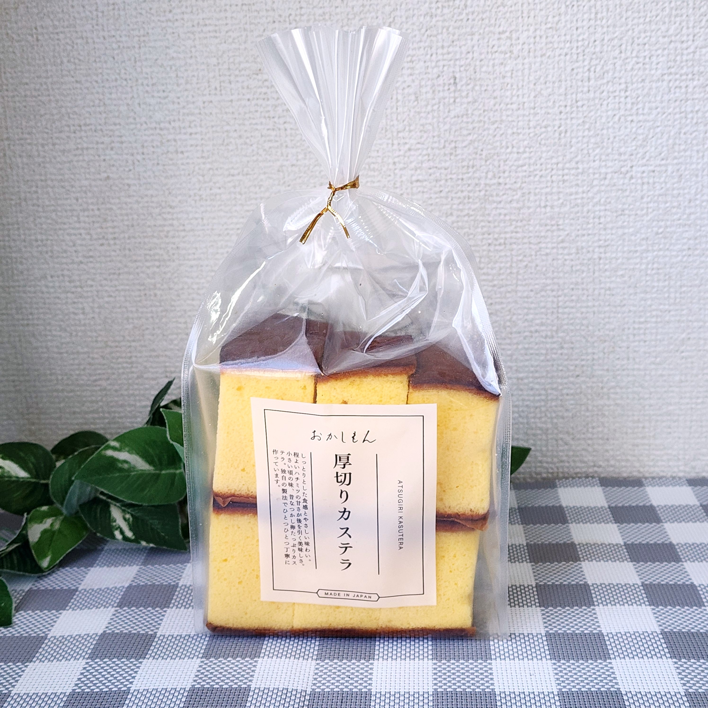 袋に入った厚切りカステラがテーブル上に置かれている。背景に緑の葉が少し見える。