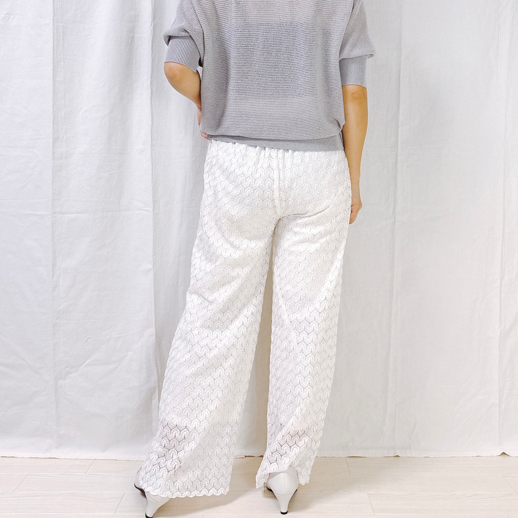 Person in a loose, textured top and wide-legged patterned pants, standing with their back to the camera on a neutral background